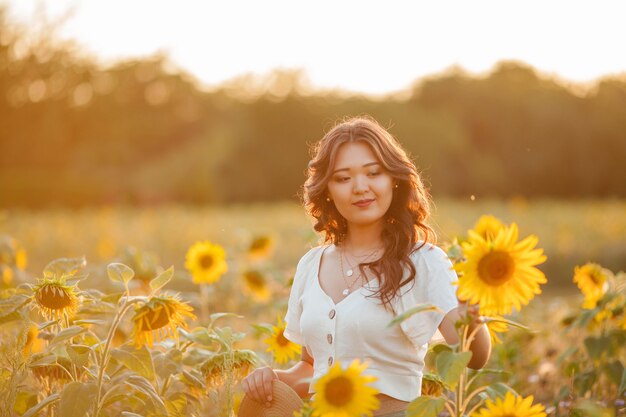 Jonge Aziatische vrouw met krullend haar in een veld met zonnebloemen bij zonsondergang.