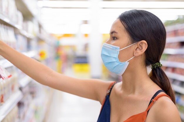 Jonge aziatische vrouw met masker voor bescherming tegen de uitbraak van het coronavirus die bij de supermarkt winkelen