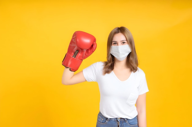 Jonge Aziatische vrouw met medisch maskerbescherming tegen coronavirus COVID19 vecht met bokshandschoenen gezond en veiligheidszorgconcept op gele achtergrond geïsoleerde studio opname kopieerruimte