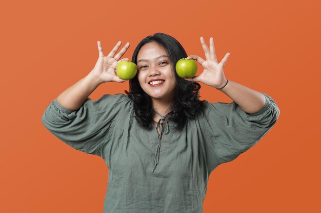 Jonge aziatische vrouw met mooie glimlach die verse groene appel houdt, die gezonde voeding bevordert