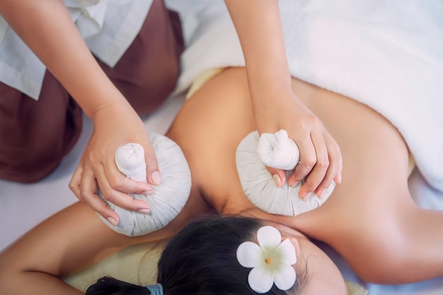 Jonge Aziatische vrouw neemt Thaise kruidenbal hete kompresmassage in een authentieke, authentieke spa