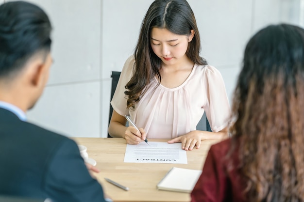 Jonge Aziatische vrouw ondertekent het contract met twee managers met positieve beweging