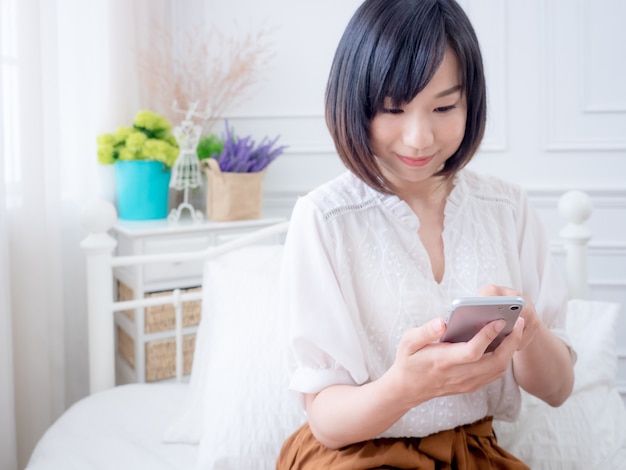 Jonge Aziatische vrouw op bed met behulp van telefoon