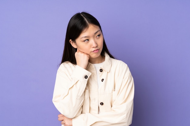 Jonge Aziatische vrouw op paarse muur met moe en verveeld meningsuiting