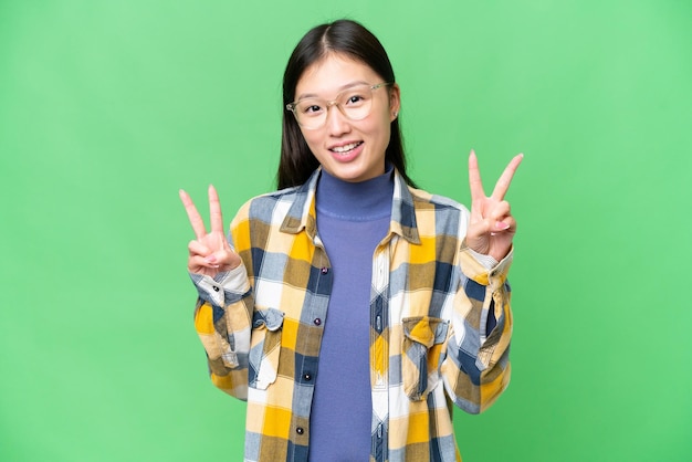 Jonge Aziatische vrouw over geïsoleerde chroma key achtergrond met overwinningsteken met beide handen