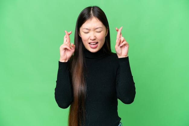 Jonge Aziatische vrouw over geïsoleerde chroma key achtergrond met vingers over elkaar
