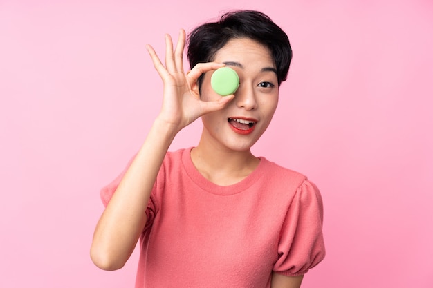 Jonge aziatische vrouw over geïsoleerde roze muur die kleurrijke franse macarons houdt