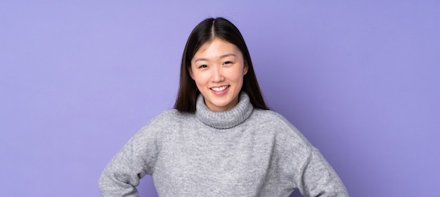 Foto jonge aziatische vrouw over muur poseren met armen op heup en glimlachen