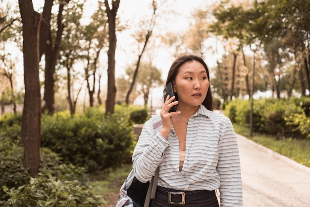 Jonge Aziatische vrouw praten via de telefoon in stadspark op zonnige zomerdag