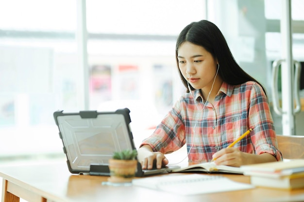 Jonge aziatische vrouw studeert achter de laptop en gebruikt een koptelefoon bij offsitexA