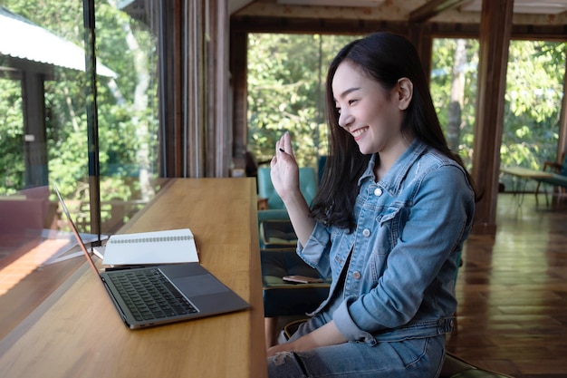 Foto jonge aziatische vrouw videobellen met haar vriend op laptop in coffeeshop online werken