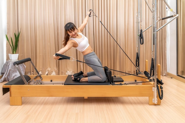 Foto jonge aziatische vrouw werkt aan een pilates reformer machine tijdens haar gezondheidsoefenopleiding