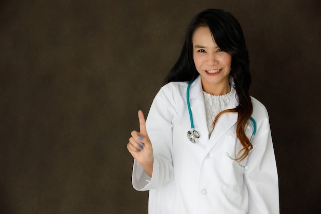 Jonge Aziatische vrouwelijke arts met stethoscoop pose ziet eruit als het aanraken van de onzichtbare of virtual reality-knop op een donkergrijze achtergrond