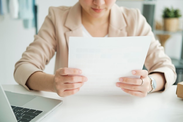 Jonge Aziatische vrouwelijke freelancer zit een rapport op papier te lezen in online kledingwinkelxA