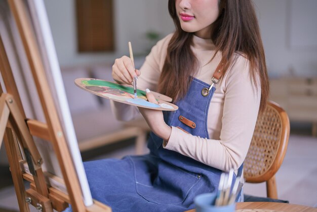 Jonge Aziatische vrouwelijke kunstenaar die een penseel gebruikt om kleur op palet te mengen om een schilderij op doek te maken