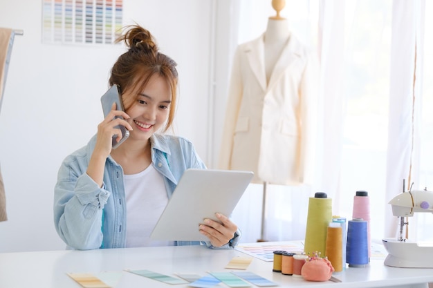 Jonge aziatische vrouwelijke professionele modeontwerper praat aan de telefoon met de klant.