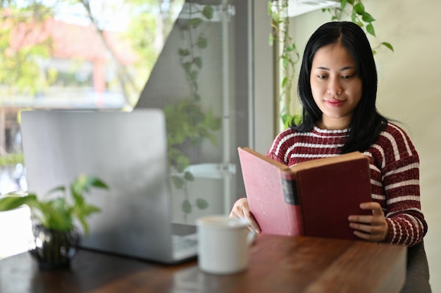 Jonge Aziatische vrouwelijke student die zich concentreert op het lezen van een boek of leerboek