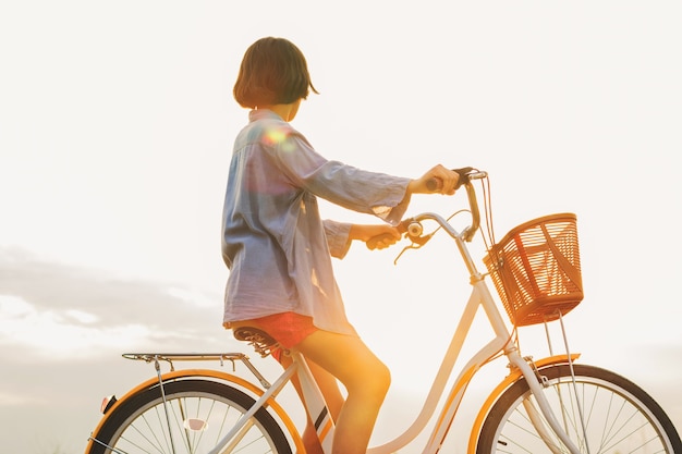 Jonge Aziatische vrouwen berijdende fiets bij park met zonsondergang