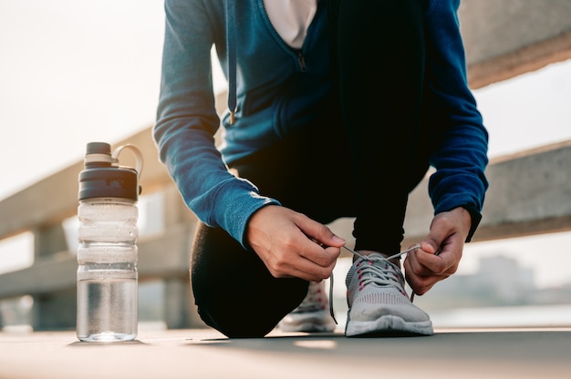 Jonge aziatische vrouwen die hun handen gebruiken om hun schoenen te binden die joggen in de ochtendtraining in de stad