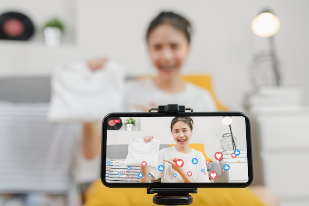 Jonge Aziatische vrouwen die kleren en verkoop online op sociaal met smartphone tonen aan klanten van huis. Netwerk technologie concept.