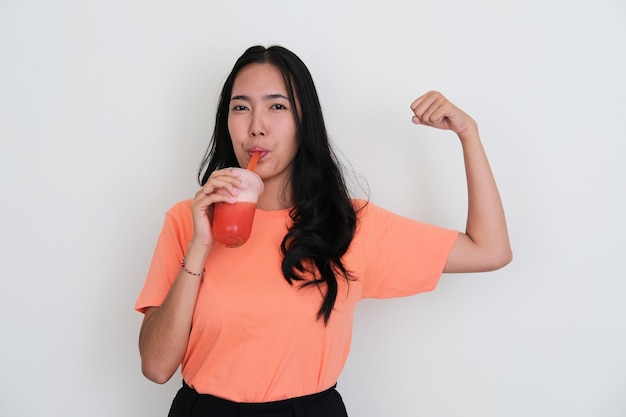 Jonge aziatische vrouwen die zijn biceps-spier laten zien terwijl ze een gezond drankje drinken