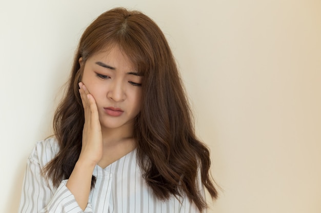 Jonge Aziatische vrouwen hebben gevoelige tanden, kiespijn, tandbederf of ontstoken tandvlees op een heldere achtergrond. Gezondheid en zieke mensen concept.