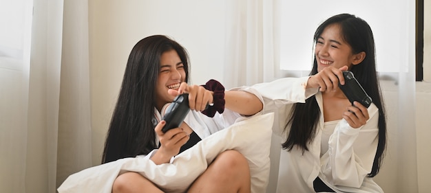 Jonge aziatische vrouwen spelen een videogame terwijl ze samen in de comfortabele slaapkamer zitten.