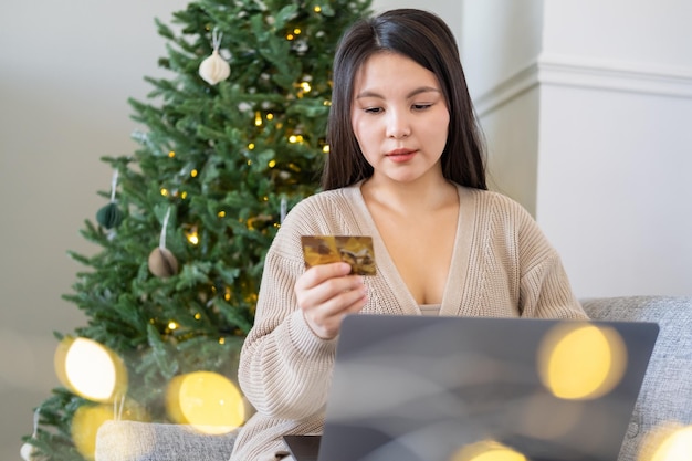 jonge aziatische vrouwen winkelen online verkoop met creditcard met behulp van laptop op de bank thuis, kerstmis