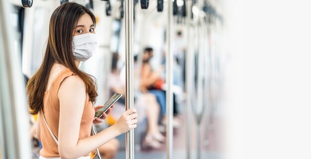 Jonge aziatische vrouwenpassagier die chirurgisch masker draagt en camera in metro bekijkt