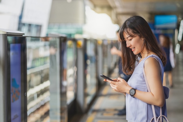 Jonge Aziatische vrouwenpassagier die sociaal netwerk via slimme mobiele telefoon gebruikt