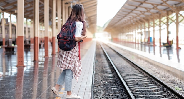 Jonge aziatische vrouwenreiziger met rugzak in de spoorweg, rugzak en hoed bij het treinstation met een reiziger, reisconcept. Vrouw reiziger toerist wandelen op treinstation