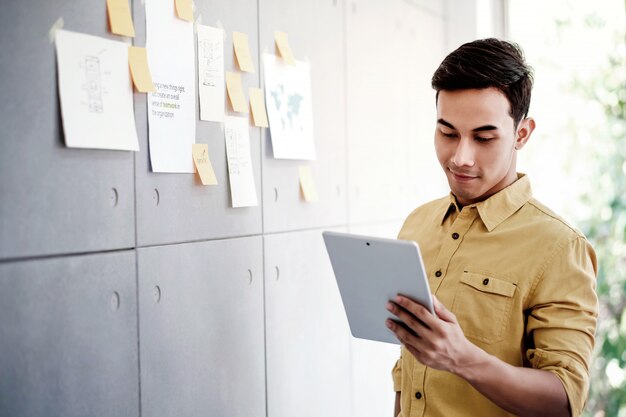 Jonge Aziatische Zakenman die aan Digitale Tablet in Bureauvergaderzaal werken.