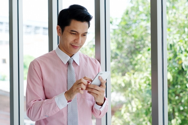 Jonge Aziatische zakenman met behulp van slimme telefoon op kantoor