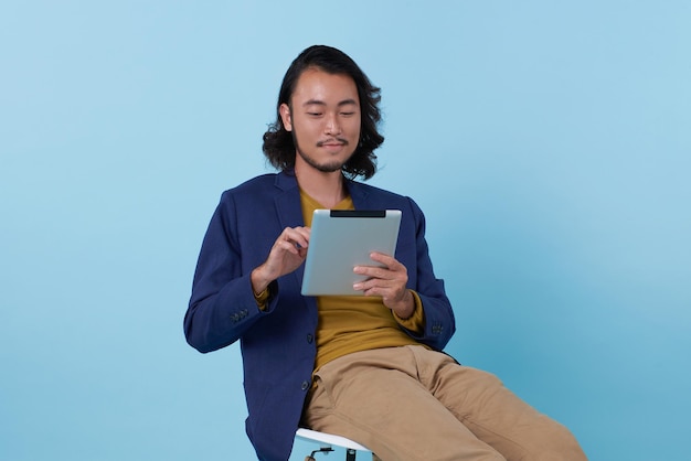 Jonge Aziatische zakenman met behulp van tablet zittend op stoel isoleren op blauwe achtergrond