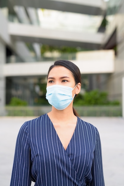 Jonge Aziatische zakenvrouw denken met masker voor bescherming tegen de uitbraak van het coronavirus in de stad