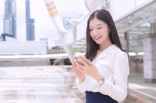 Jonge Aziatische zakenvrouw die glimlacht, speelt en kijkt naar smartphone in haar handen