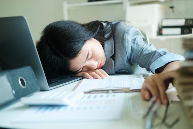 Jonge aziatische zakenvrouw vermoeide vrouwenslaap op bureau met laptop alleen op de werkplek