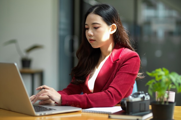 Jonge aziatische zakenvrouw zit aan haar bureau in een lichte, moderne kantoorwerkruimte die op laptop werkt