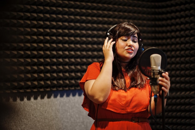 Jonge aziatische zangeres met microfoon die lied opneemt in muziekstudio