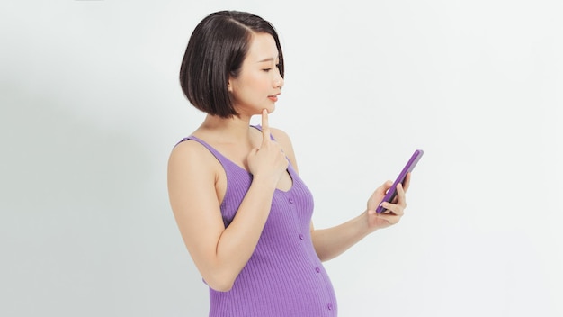 Jonge Aziatische zwangere vrouw gebruikt mobiele telefoon over wit