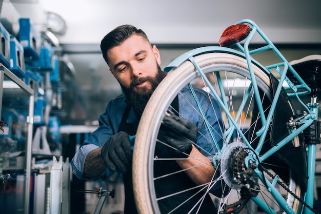 Jonge baard fietsenmaker repareren van fietsen in een werkplaats.