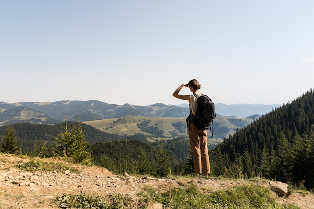 Jonge backpacker toeristische jonge vrouw staat bovenop de berg en kijkt naar heuvels met bossen en weiden