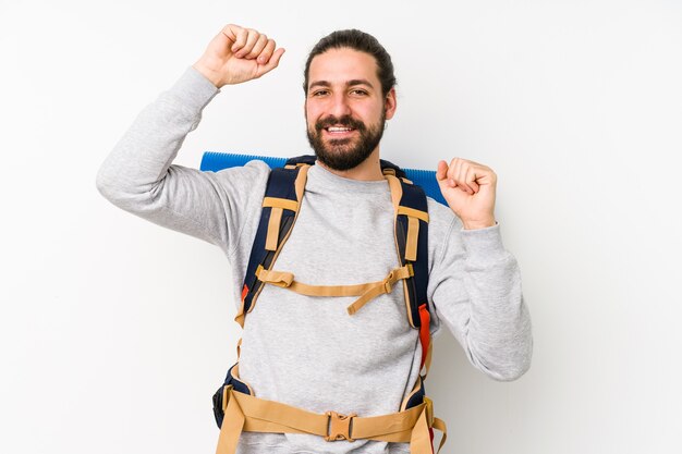 Jonge backpackermens die op een witte muur wordt geïsoleerd die een speciale dag viert, springt en heft wapens op met energie.