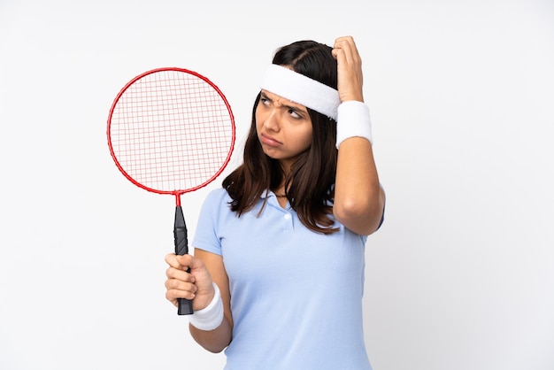 Jonge badmintonspelervrouw over geïsoleerde witte achtergrond die twijfels heeft terwijl het hoofd krabben