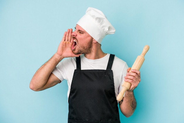Jonge bakker man geïsoleerd op blauwe achtergrond schreeuwen en houden palm in de buurt van geopende mond