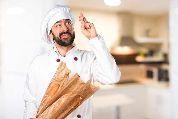 Jonge bakker met wat brood en met zijn vingers kruist in de keuken