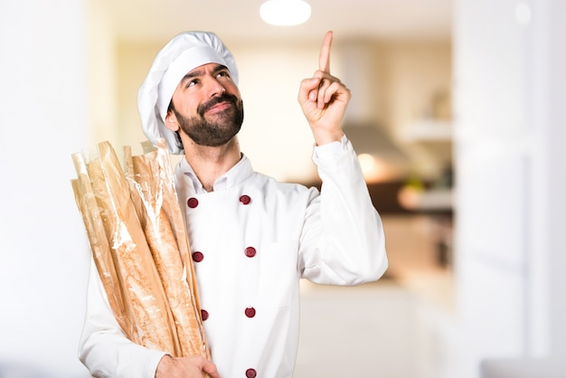 Jonge bakker met wat brood en wijst in de keuken