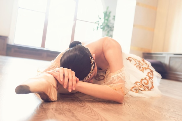 Jonge ballerina in een witte tutu die zich opwarmt voor de training, liggend op de studiovloer