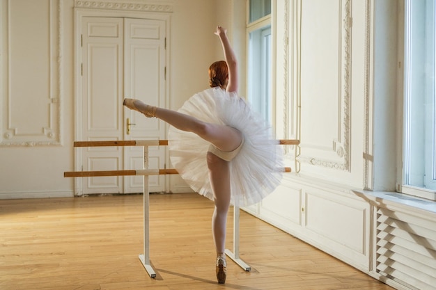 Jonge ballerina in tutu rok strekt zich uit bij het oefenen van balletposities bij het dansen in de buurt van de balletbarre in