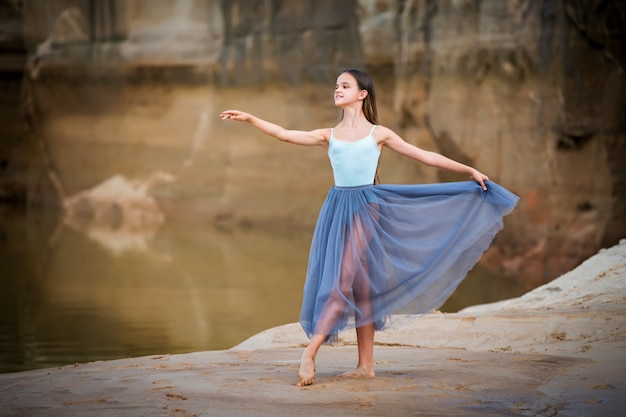 Jonge ballerina staat in een sierlijke pose aan de rand van een zanderige klif